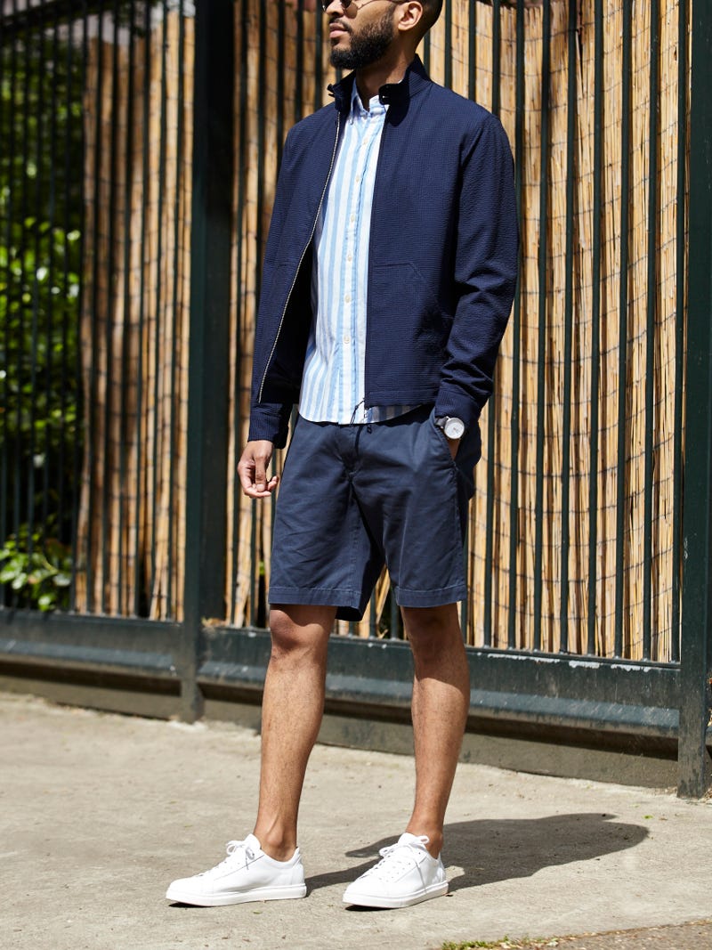 Men's outfit idea for 2022 with harrington jacket, short-sleeved patterned shirt, navy shorts, white sneakers. Suitable for spring and summer.