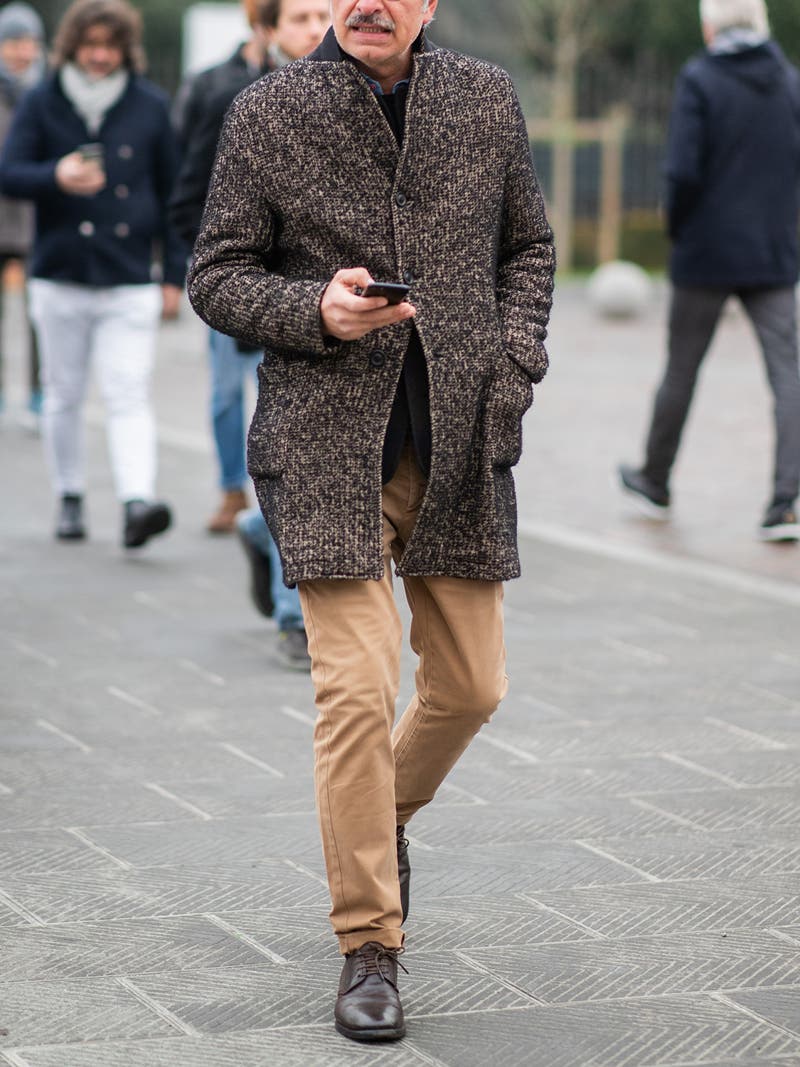 Men's outfit idea for 2022 with brown single-breasted overcoat, navy crew neck knitted sweater, blue denim shirt, stone chinos, oxford / derby shoes. Suitable for fall and winter.