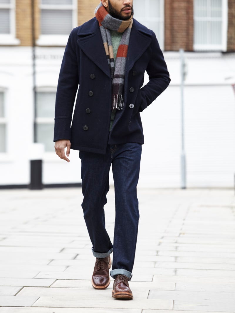 Men's outfit idea for 2022 with pea coat, bold coloured crew neck jumper, dark blue jeans, multicoloured patterned knitted scarf, brown brogues. Suitable for autumn and winter.