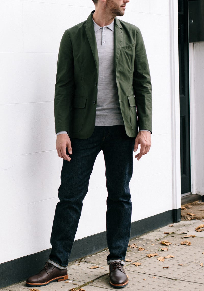 Men's outfit idea for 2022 with utility jacket, gray long-sleeved polo, dark blue jeans, oxford / derby shoes. Suitable for spring and fall.